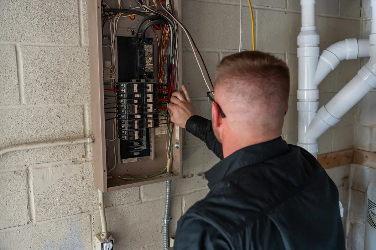 Tim Sky troubleshooting a circuit at an open panel in a basement